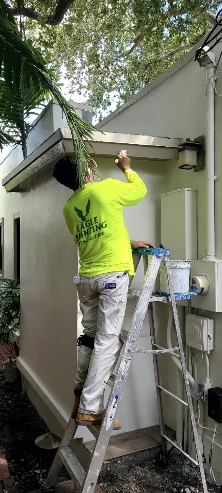 Eagle Painting crew member on a ladder cutting in trim on a stucco house