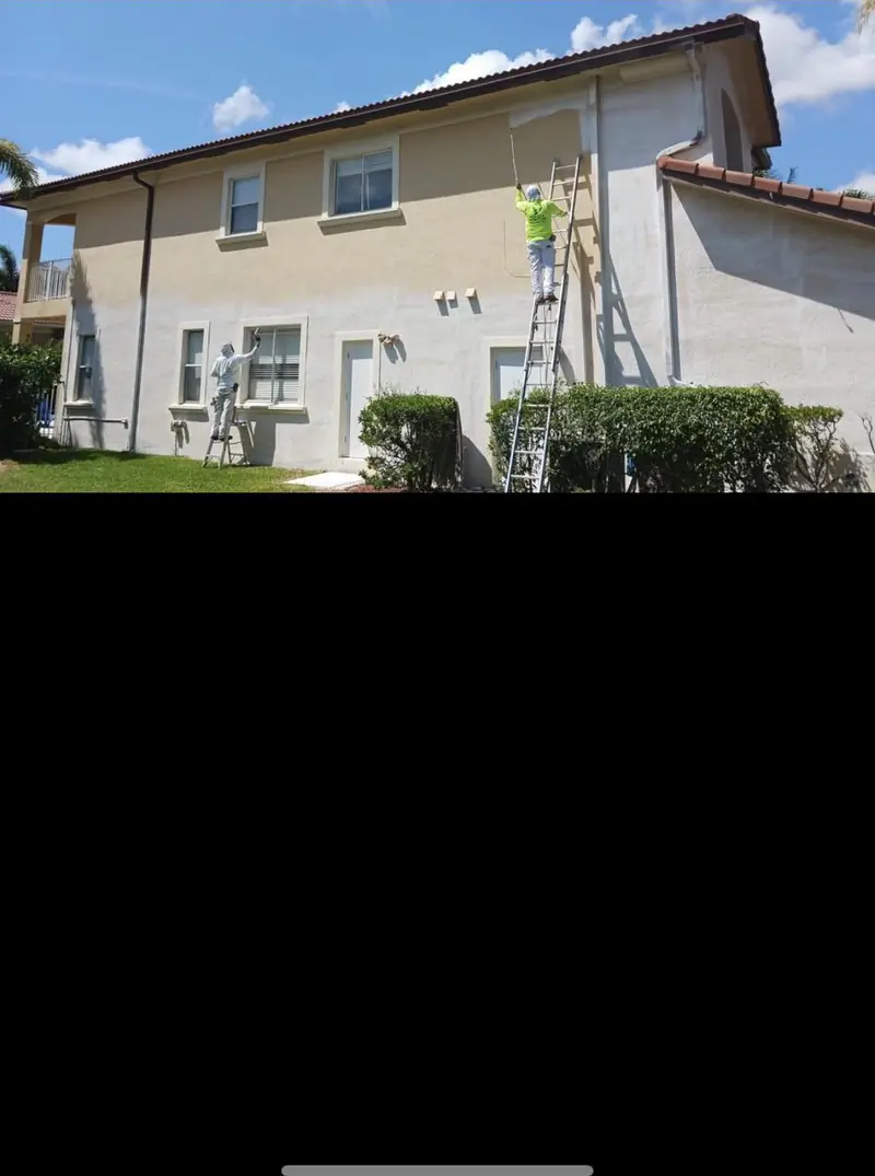 Stucco home in Broward County mid-repaint with a ladder at the wall